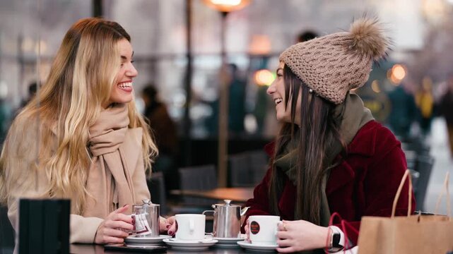 Video of two beautiful women talking while drinking coffee sitting in the bar terrace.
