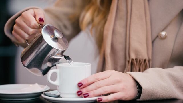 Video of close up of woman pouring herself a cup of tea on a bar terrace.