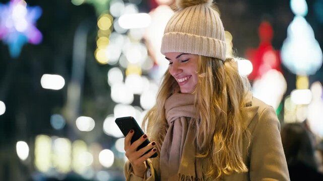 Video of pretty woman using smartphone while walking on the city street in winter with shopping bag.