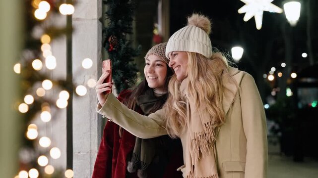 Video of two beautiful women taking a photo with smartphone of a shop window at night in winter.