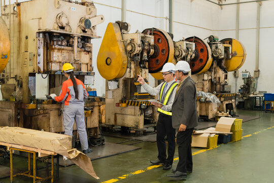 Engineer Pointing Out Machine Detail To Senior Manager Along Punch Press Row supporting efficient production and workplace safety inside a busy metalworking factory setting