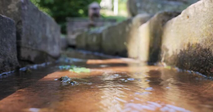 Low angle view of fresh clear water stream flowing inside a stone trough channel of an outdoor fountain on sunny day