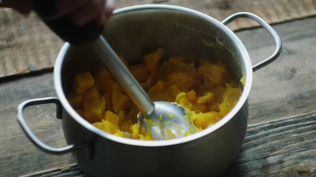Cooking pumpkin puree soup. Mixer mashes cooked pumpkin in pot