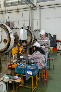 Female machine operator feeds metal stock into an old power press while an engineer checks data on a tablet beside her