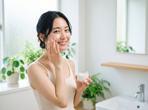 洗面所でフェイスクリームを肌になじませ笑顔を見せる女性