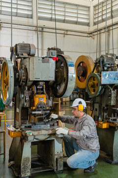 Full Length View Of Machine Operator Crouching Beside Power Press Flywheels ensuring precision and quality in a modern industrial manufacturing environment with heavy machinery