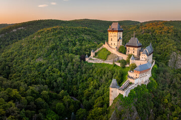 Obraz premium Aerial view of iconic gothic royal Karlstejn Castle surrounded by lush green forests at golden hour sunset, UNESCO candidate site, Central Bohemia, Czech Republic ( Hrad Karlštejn-Česká Republika )