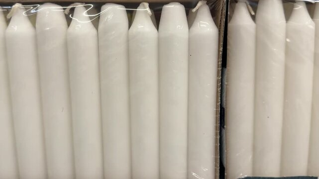 Bundles of white candles sealed in transparent wrapping are arranged for sale in a retail display, offering practical lighting solutions for homes, celebrations, decoration and power outages. Close up