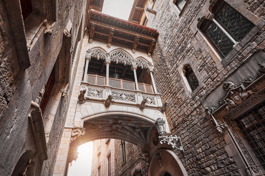 Barcelona, Spain. Barri Gotic Quarter. Antique Bridge between stone walls of medieval buildings in in old town. Famous touristic landmark and travel destination. Sunset evening street perspective.