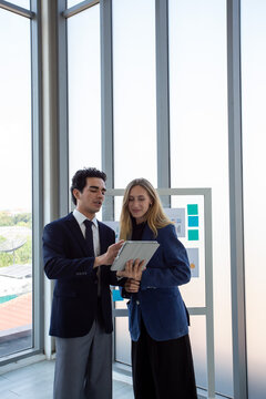 Two business professionals discussing marketing strategy and business analytics in front of a glass board with charts and sticky notes.Corporate colleagues collaborating on project planning,