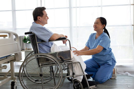 Smiling nurse giving medication and a glass of water to an elderly patient sitting in a wheelchair in a hospital room. Senior healthcare, nursing care, rehabilitation, compassion