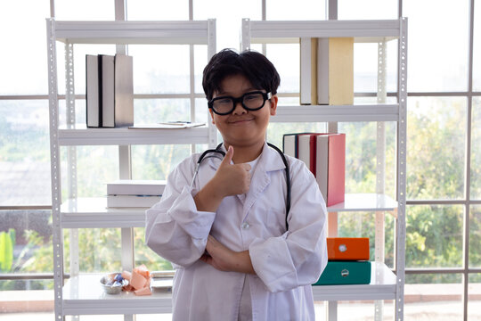 Young Asian boy in glasses and lab coat acting as a doctor. 
Portrait of a confident Asian child in a white coat with a stethoscope for role play.