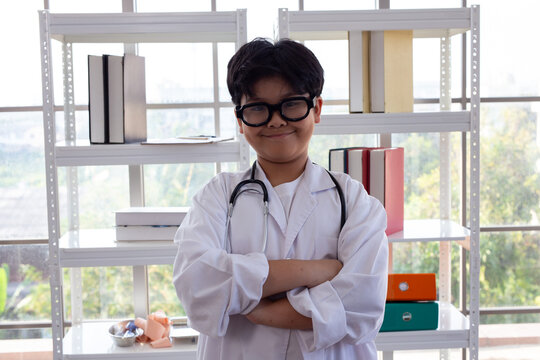 Young Asian boy in glasses and lab coat acting as a doctor. 
Portrait of a confident Asian child in a white coat with a stethoscope for role play.