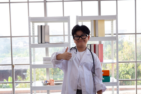 Young Asian boy in glasses and lab coat acting as a doctor. 
Portrait of a confident Asian child in a white coat with a stethoscope for role play.
