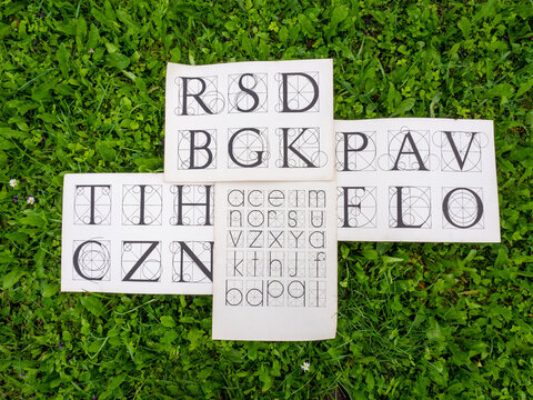 A collection of geometric alphabet design sheets displayed on lush green grass, featuring uppercase and lowercase letter constructions based on circles, grids, and geometric proportions