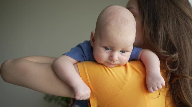 Tender moment showing a loving mother holding her curious infant son on her shoulder, providing comfort and care as the newborn looks around before gently falling asleep