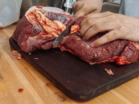 Preparing raw beef by trimming and cutting meat on a cutting board before making homemade minced meat.