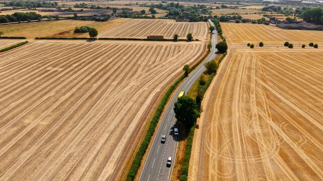 Aerial view of rural road with yellow bus traveling through harvested farmland. Countryside transportation crossing golden agricultural fields after harvest with scenic landscape and patchwork