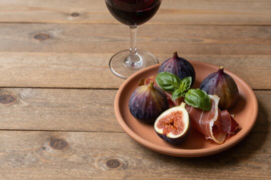 prosciutto and fresh figs on rustic plate with red wine on wooden table inviting gourmet snack
