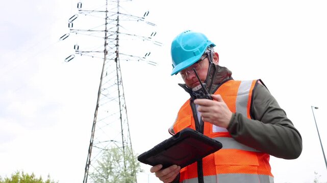 Electrical safety inspector entering technical audit data into a tablet application and communicating real-time report status via portable walkie-talkie radio. Power engineer.