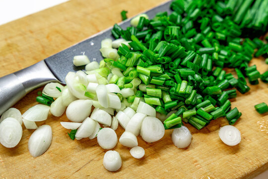 Chopped green and white spring onions on wooden cutting board