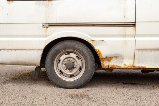 Old white van with heavy rust and corrosion on side panel and wheel arch