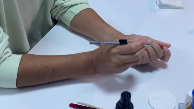 A focused person carefully pushes cuticles using a metal tool. The hands work gently at a clean white desk, creating a calm and relaxed mood.