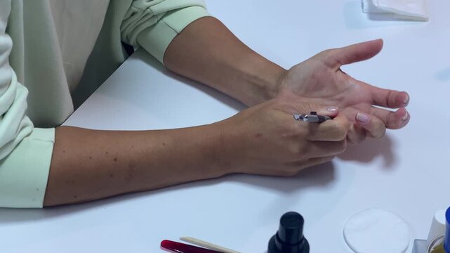 A calm person gently pushes back her cuticles with a metal tool. She carefully manicures her nails at a bright white desk. This peaceful routine creates a relaxed mood.
