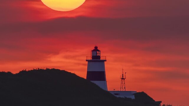 A dramatic orange and red sunset sky behind the silhouette of Fuguijiao Lighthouse on the coast of Shimen, New Taipei City, Taiwan.