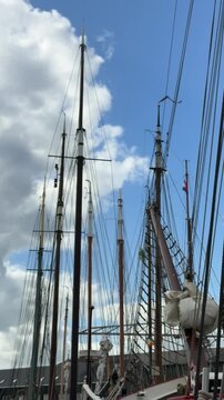 Slow camera movement past sailboat masts ropes and rigging beneath moving clouds in the historic harbor of Monnickendam Netherlands.