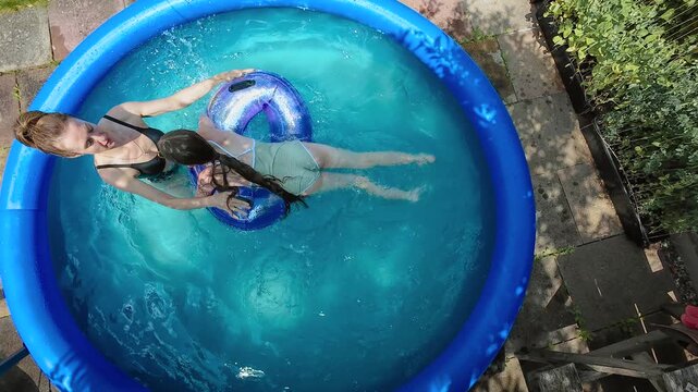 Extreme summer heat relief. Woman and girl enjoying inflatable home pool during climate warming. Backyard family cooling supporting heatwave survival, critically high temperatures, outdoor refreshment