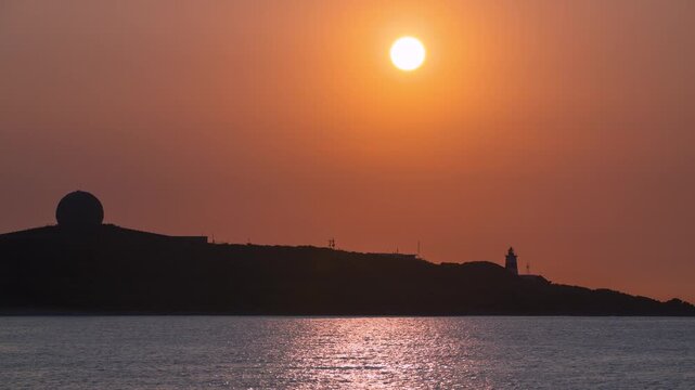 A beautiful sunset with an orange sky over the silhouette of Fuguijiao Lighthouse and radar dome on the coast of Shimen, Taiwan.