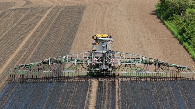 Farmer driving tractor distributing liquid manure fertilizer for crop cultivation. Organic nutrient application improving soil condition, farm performance, agricultural sustainability. Heavy farm