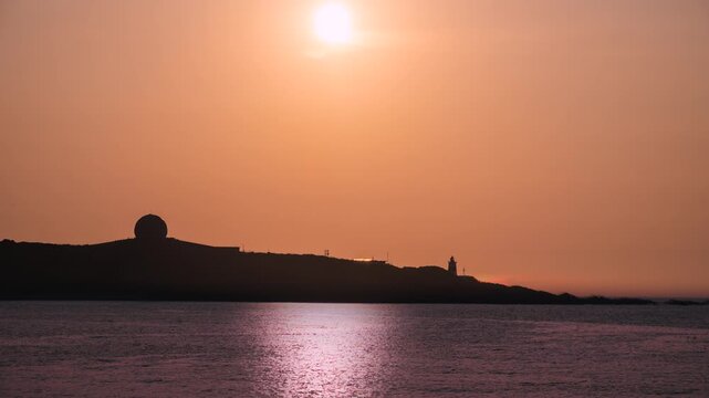 A beautiful orange sunset over the ocean with the silhouette of Fuguijiao Lighthouse and a radar dome on the coast of Shimen, Taiwan.