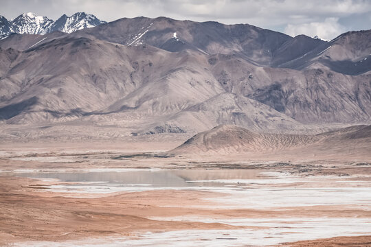 Panorama of a mountain landscape with a lake and river with clear water on a plateau in the Tien Shan Mountains in the Pamirs, mountain ridges and slopes with snow in the background