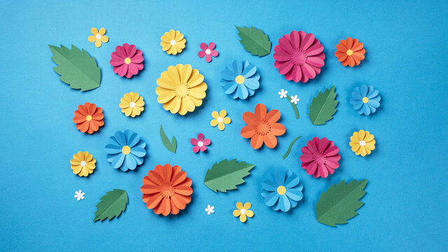 Colorful paper flowers and leaves arranged on a blue background with paper craft