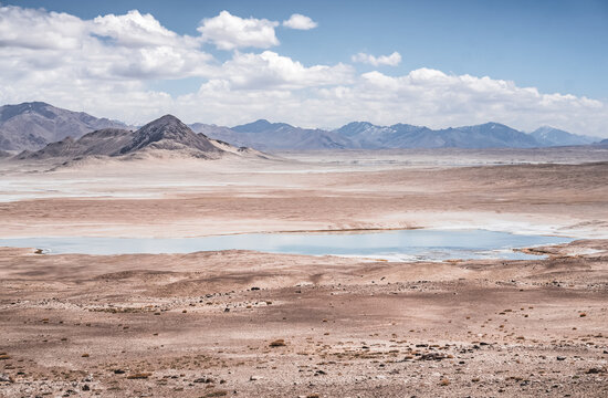 Panorama of a mountain landscape with a lake and river with clear water on a plateau in the Tien Shan Mountains in the Pamirs, mountain ridges and slopes with snow in the background