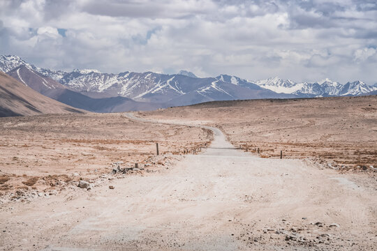 Dusty road of the Pamir Highway winds and twists in the valley of the Tien Shan mountains in Tajikistan in Pamir, landscape in the high desert mountains for background