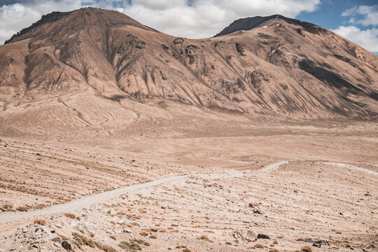 Dusty road of the Pamir Highway winds and twists in the valley of the Tien Shan mountains in Tajikistan in Pamir, landscape in the high desert mountains for background