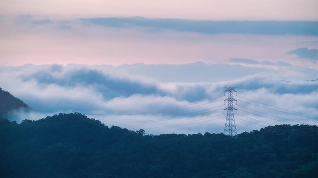 Scenic view of a high voltage power transmission tower standing on a mountain ridge surrounded by rolling clouds during sunrise in Xindian, Taiwan.