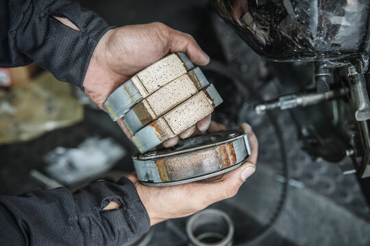 Hands of mechanic inspecting motorbike brake pads in garage