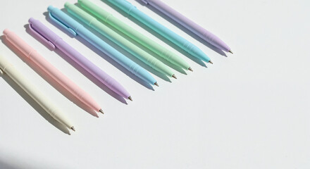 Fototapeta premium High angle view of pastel-colored ballpoint pens lined up in a neat diagonal row casting soft directional shadows on a clean white background for modern office aesthetic.