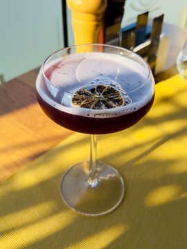 An elegant blueberry cocktail in a clear coupe glass, garnished with a slice of dried lime, set against a vibrant background.