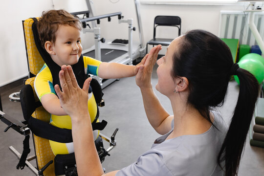 Happy boy during physical rehabilitation standing in a standing frame with his physical therapist, working on developing standing skills