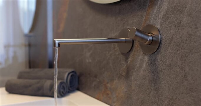 Wall mounted faucet with flowing water on a natural stone surface, static video highlights the sleek built in fixture in a luxury modern bathroom where refined materials and soft daylight create