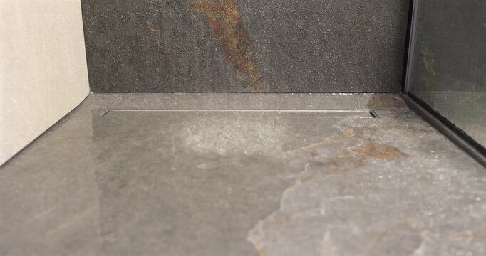 Stone shower floor with built in drain under falling water, static slow motion footage isolates the first impact of descending drops and delicate spray across the textured surface