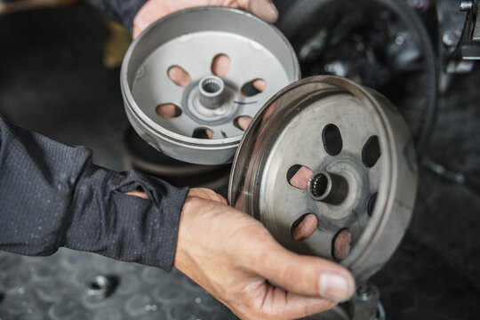 Mechanic hands holding scooter clutch bell and outer housing for inspection and maintenance in motorcycle workshop