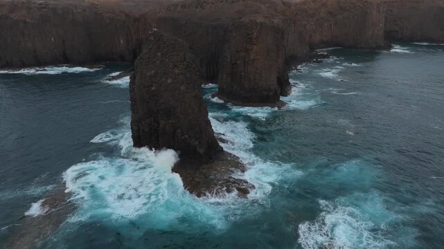 Dramatic aerial shot of Roque del Farallon, a stunning sea stack on the Gran Canaria coast, with powerful ocean waves crashing against it