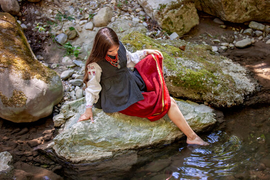Atmospheric portrait of a young Ukrainian woman in traditional embroidered clothing in a green forest, inspired by folklore, nature, legends and poetic storytelling.