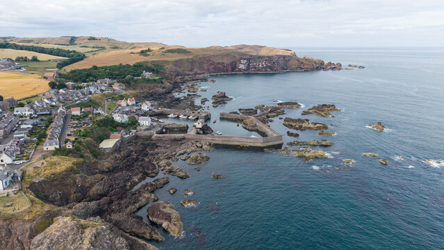 Aerial scenic panoramic view of the historic fishing village, harbour, and rugged coastline of St Abbs Head in Berwickshire, Scotland